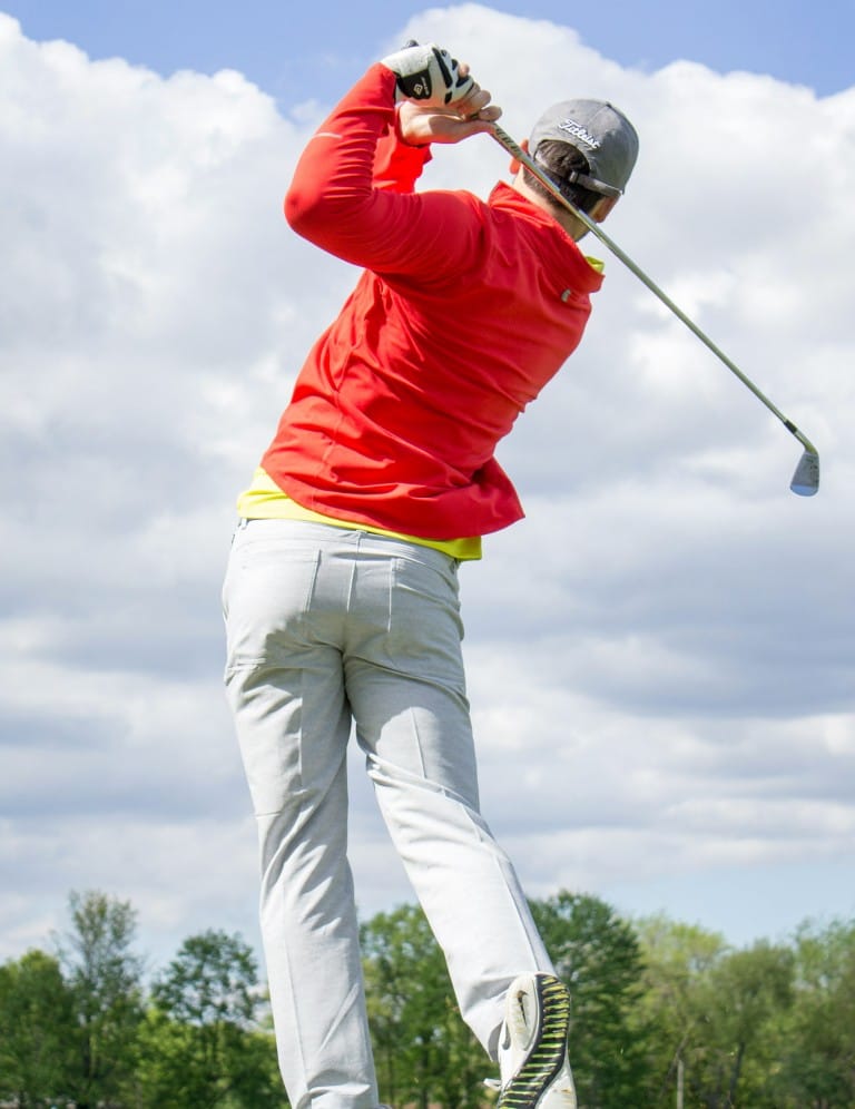 A man in a red shirt swings his golf club
