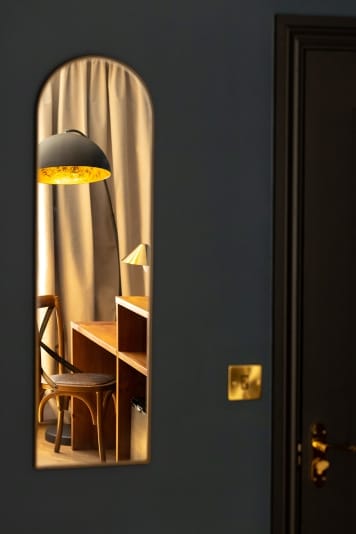 A mirror reflects a room featuring a desk and a lamp