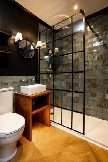 A modern bathroom featuring a glass shower, wooden vanity, and sleek black tiles